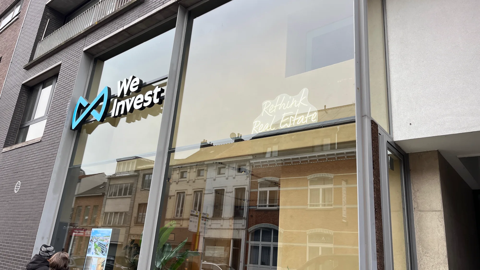 Illuminated We Invest logo on the glass front of the Leuven office