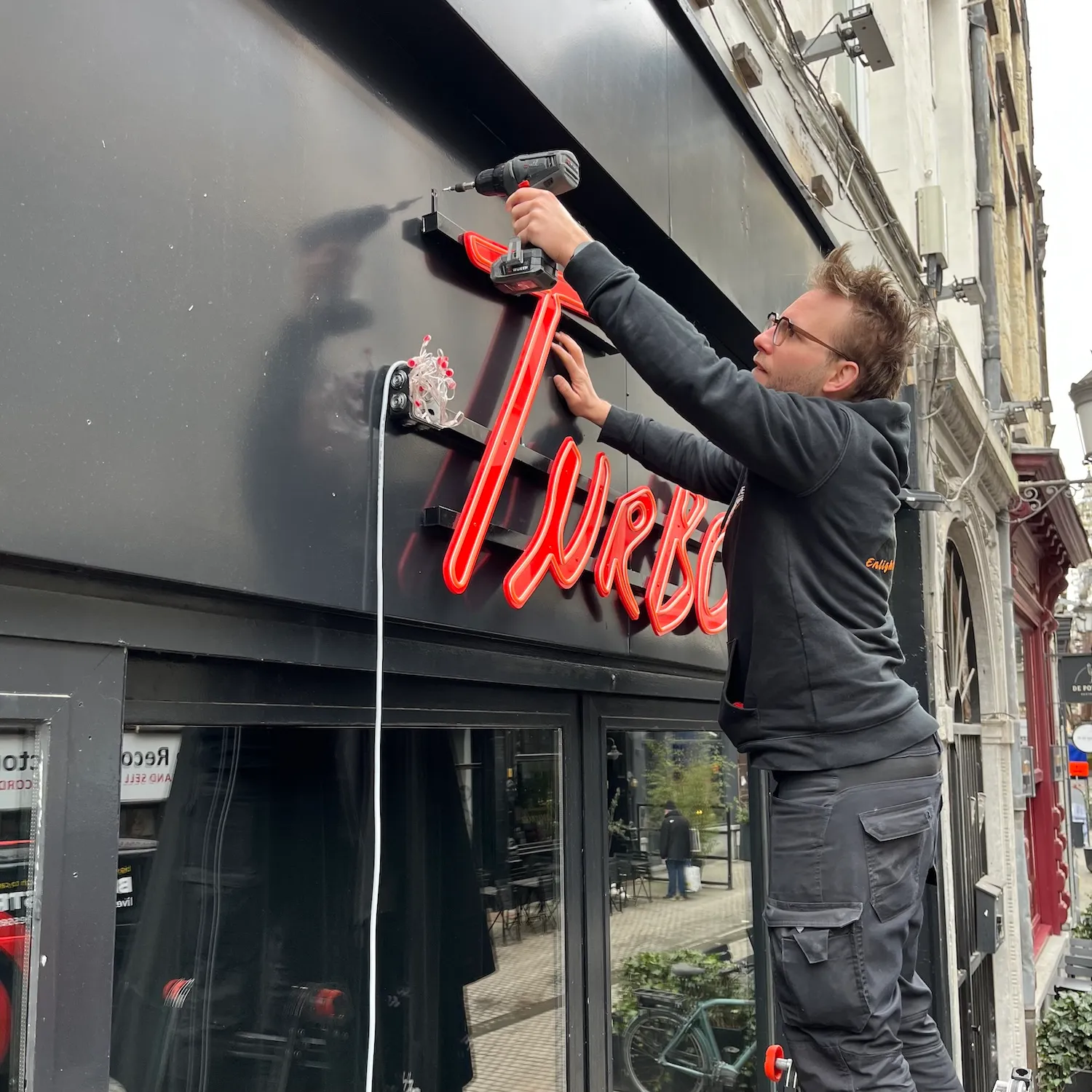 Installer fixing the red neon logo to the Turbo facade in Antwerp