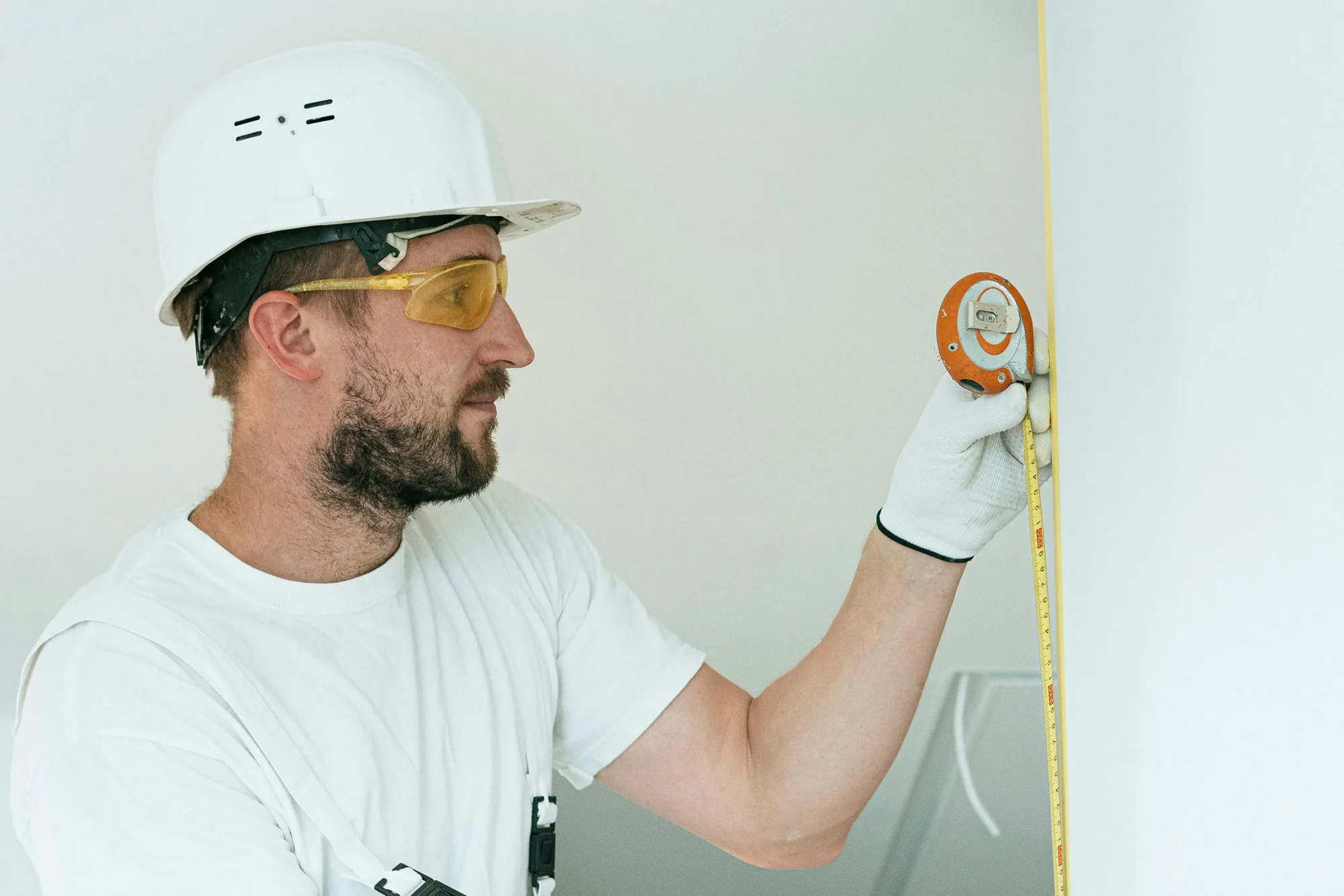 Technician in a hard hat measuring a wall with a tape measure