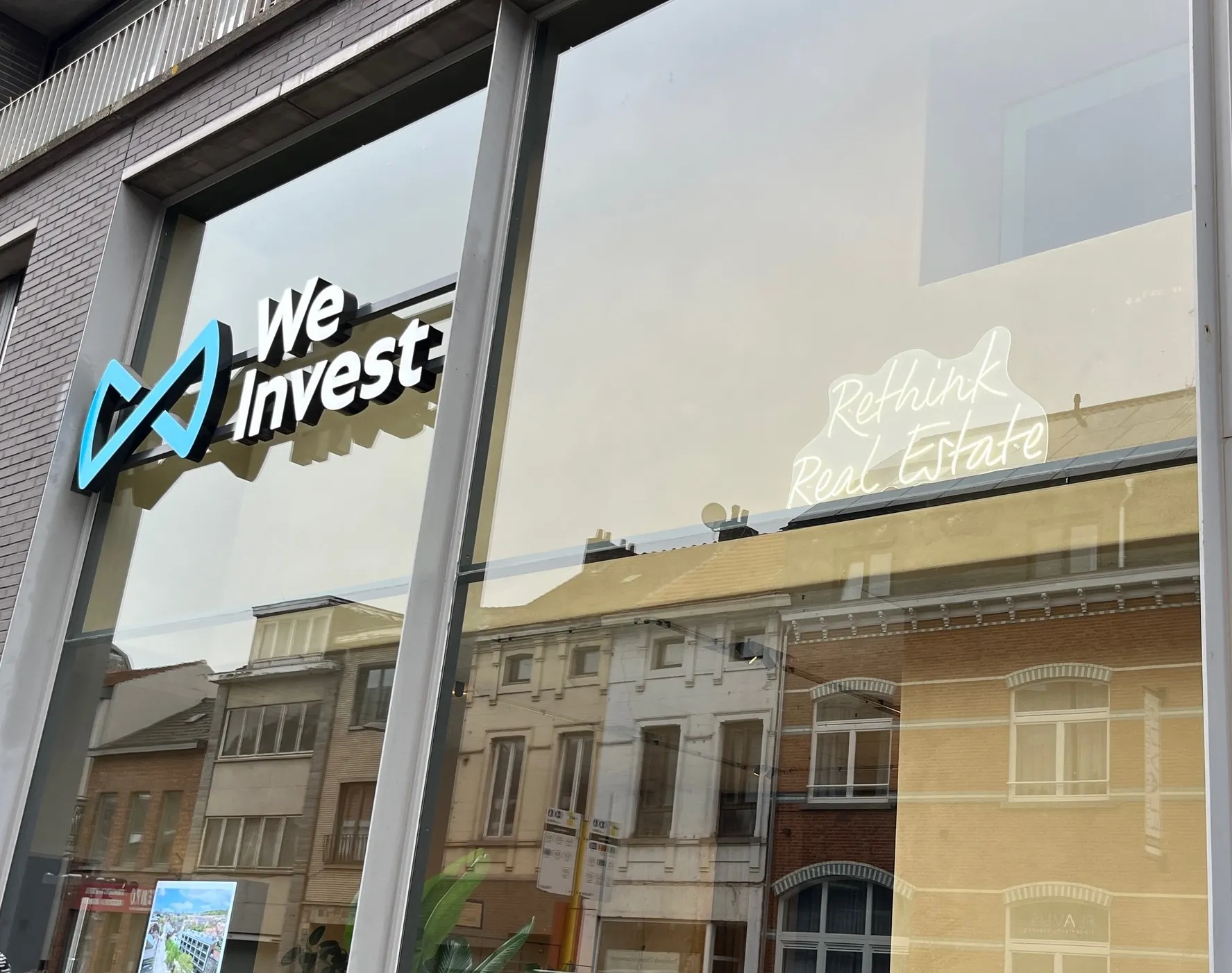 Illuminated We Invest logo on the glass facade in Leuven
