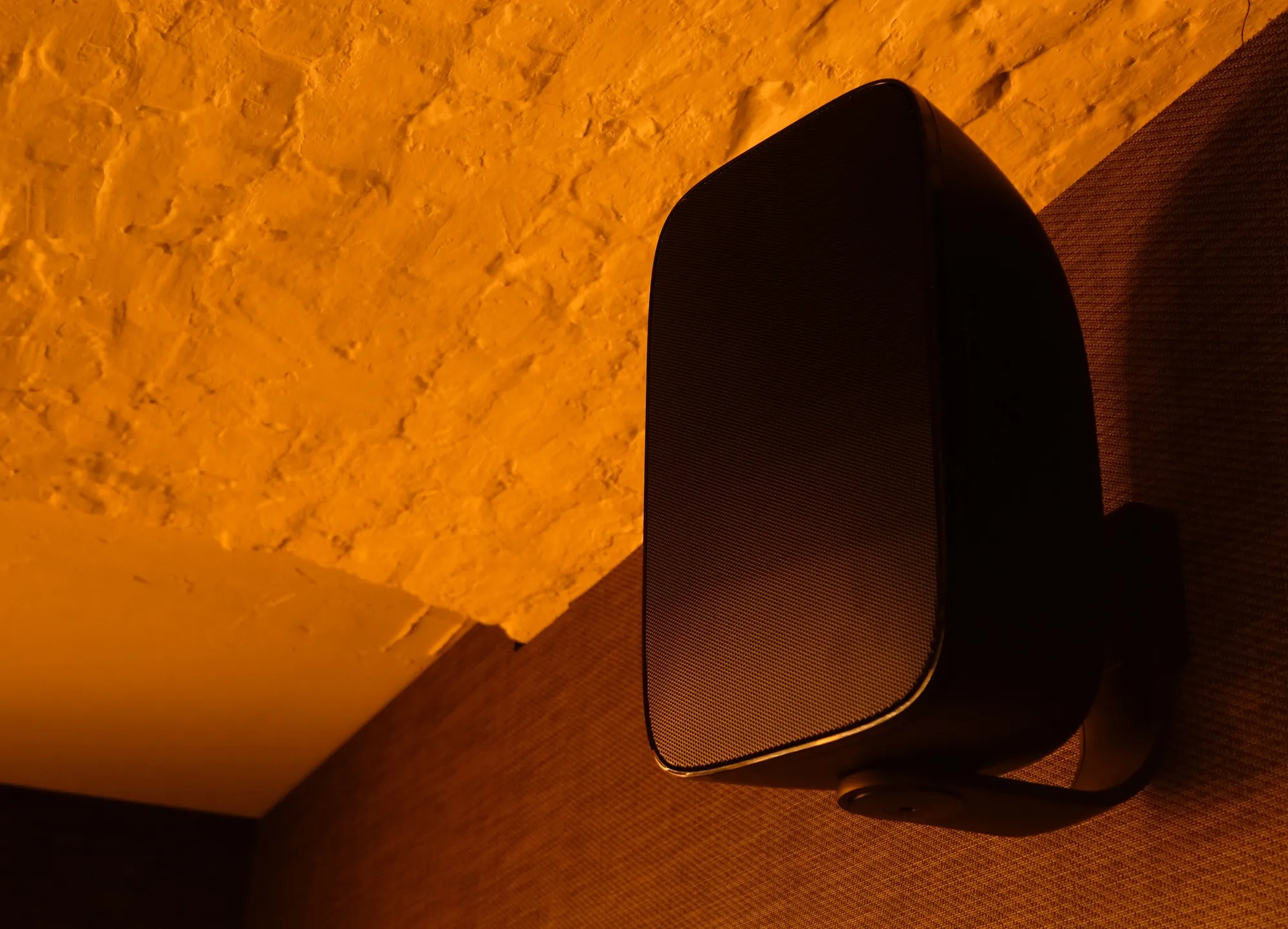 Black wall-mounted loudspeaker in a warmly lit bar