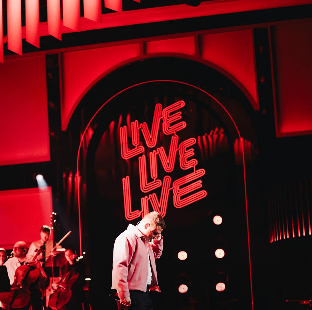 Live Live Live neon sign behind a singer in the VRT studio